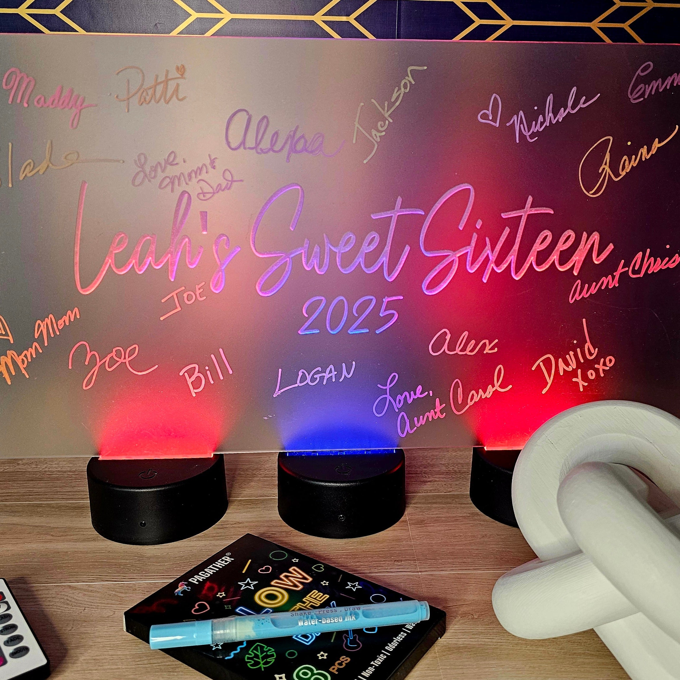 Neon sign with 'Leah's Sweet Sixteen 2025' on a stand with colorful lights, surrounded by stationery items.