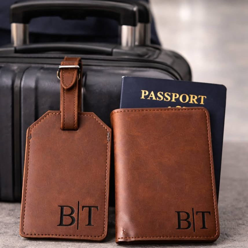 Brown leather luggage tag and passport holder with 'B|T' initials in front of a black suitcase.