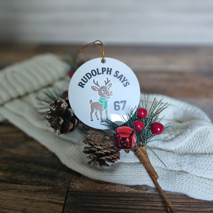 Christmas ornament with 'Rudolph Says' tag and decorative elements on a wooden surface.