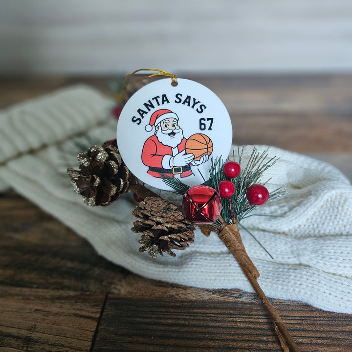 Christmas ornament with Santa Claus holding a basketball and text 'Santa Says 67' on a wooden surface.