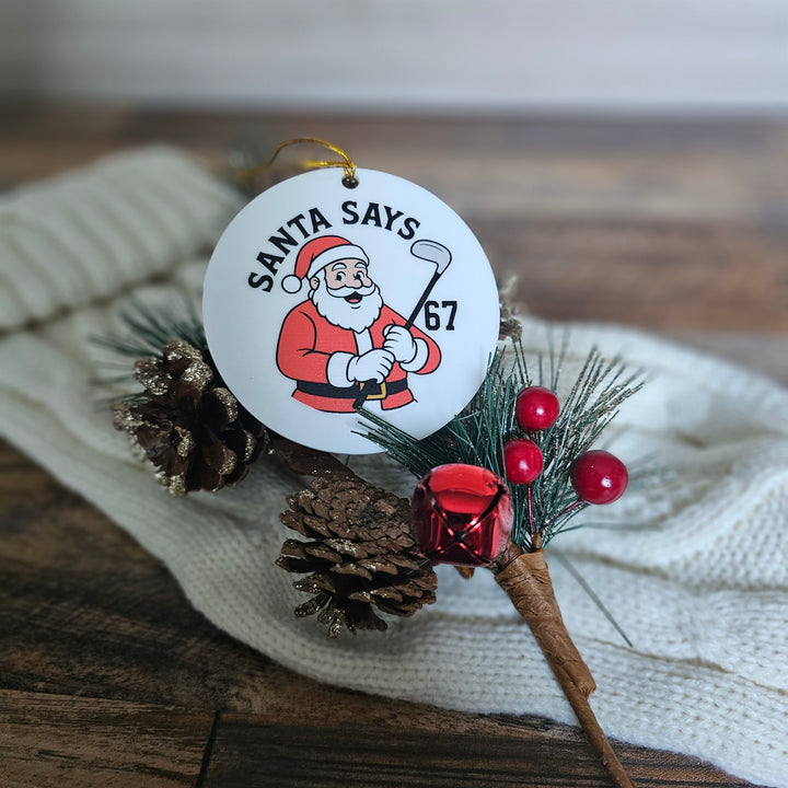 Christmas ornament with Santa Claus design and text on a wooden surface.