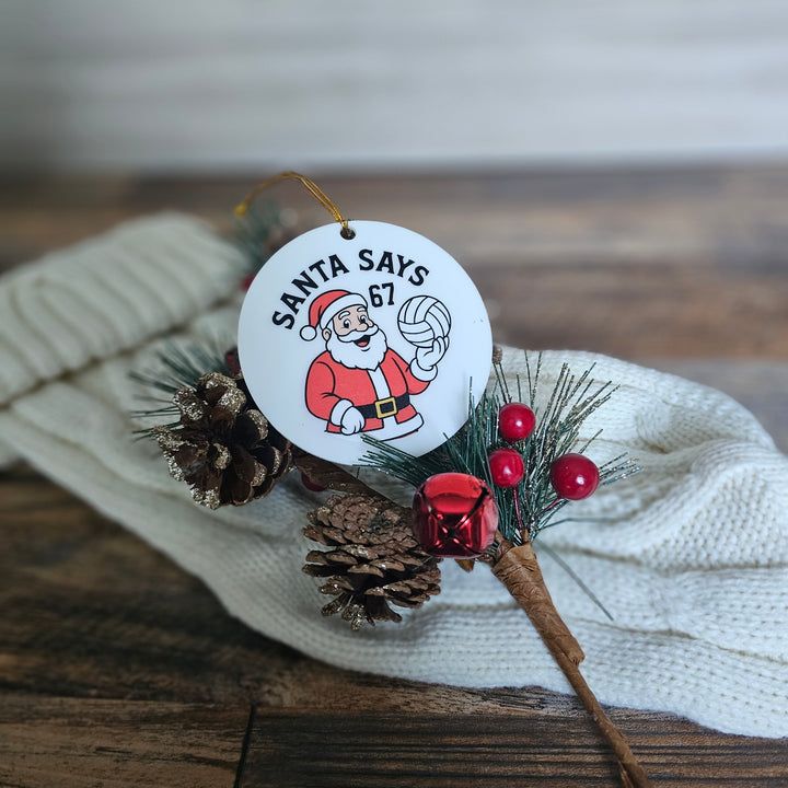Christmas ornament with Santa Claus design and text on a wooden surface.