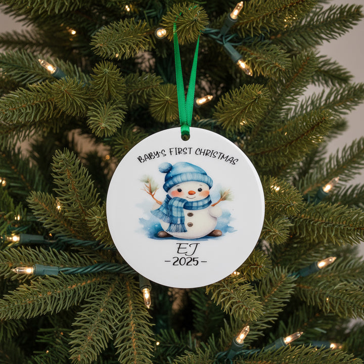 Round ceramic ornament with snowman design and text in front of Christmas tree