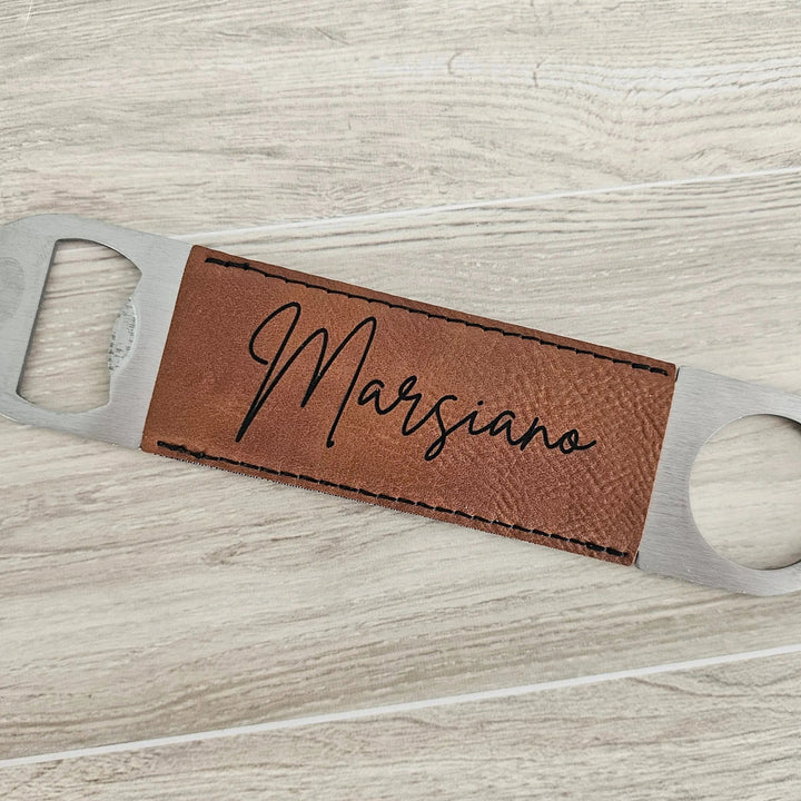 Bottle opener with brown leather tag and 'Marsiano' engraving on a light wood surface