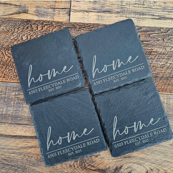 Four slate coasters with 'home' and address text on a wooden surface