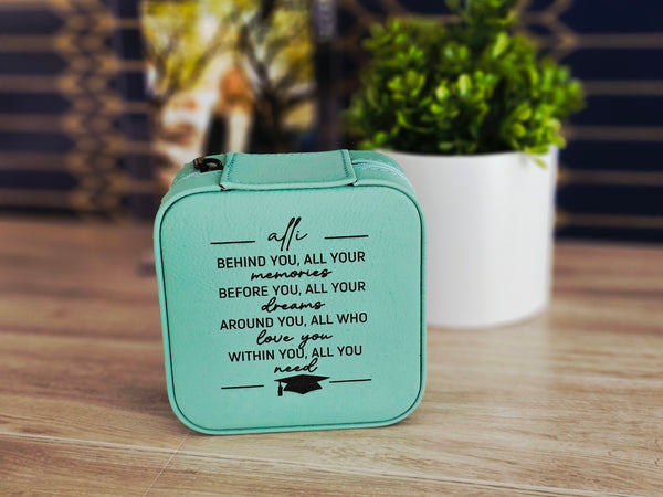 Teal graduation-themed box with motivational quote on a wooden surface with blurred plant and staircase in the background
