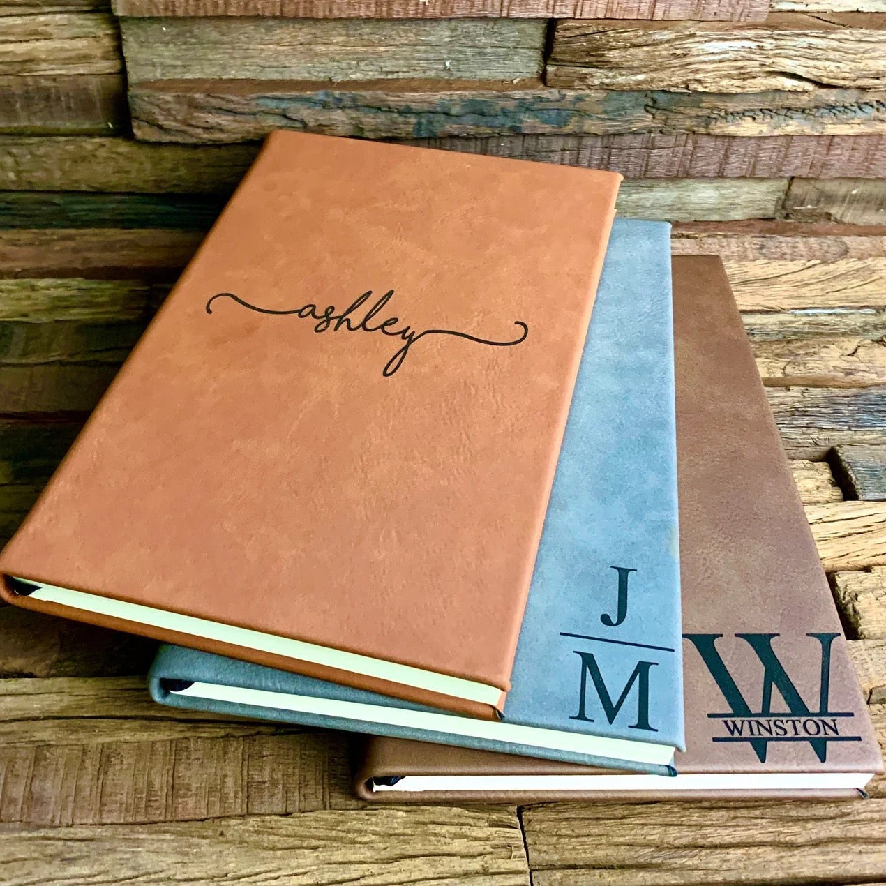 Stack of leather-bound books with personalized names on a wooden surface