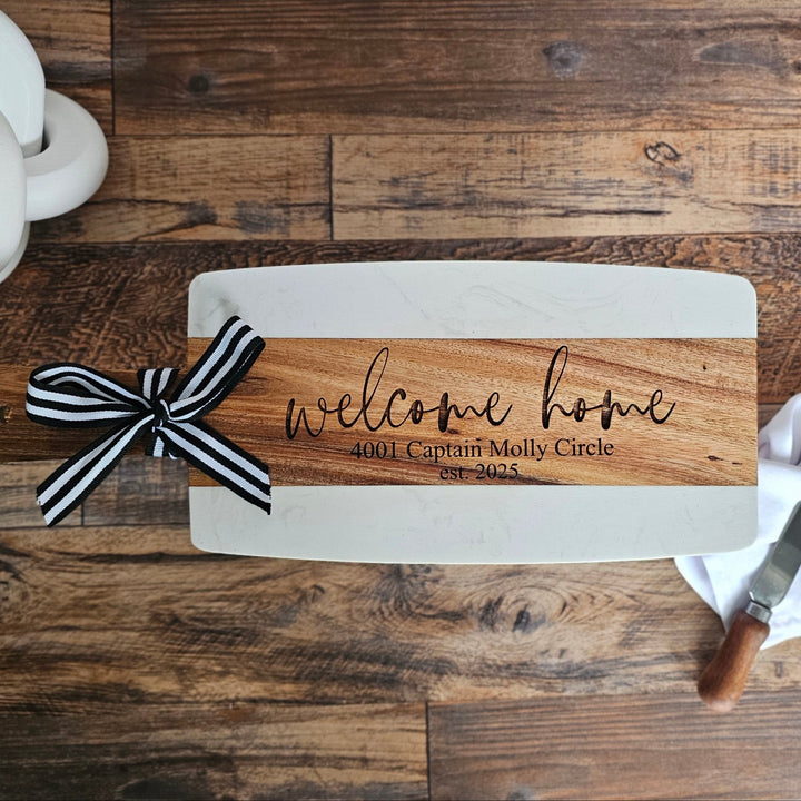 Wooden sign with 'welcome home' text and a black and white ribbon on a wooden floor.