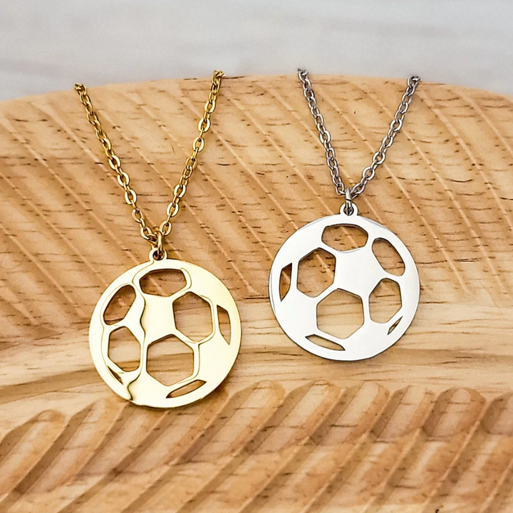 Two gold and silver soccer ball pendants on chains against a wooden background
