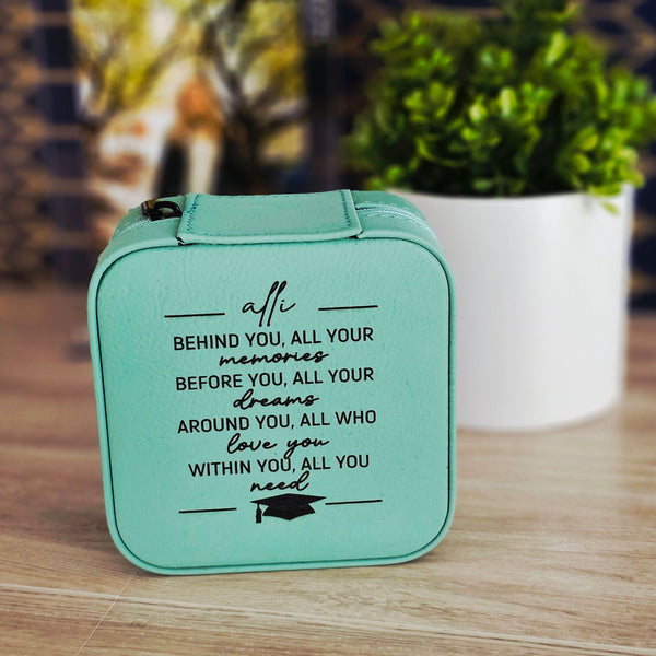 Teal graduation-themed box with motivational quote on a wooden surface with blurred plant and staircase in the background