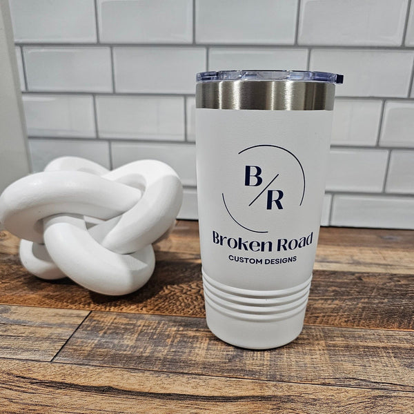 White tumbler with 'Broken Road' branding on a wooden surface with a white tile background